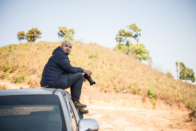 Jeune photographe assis sur son pick-up photographiant en montagne.