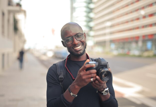 Jeune photographe masculin africain attrayant avec un appareil photo dans une rue sous la lumière du soleil