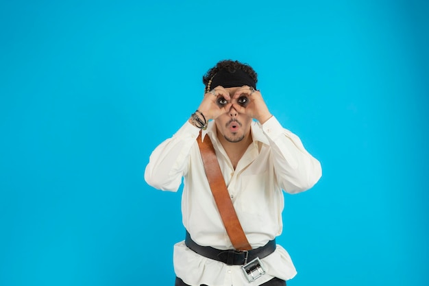 Jeune pirate utilisant ses mains comme jumelles et debout sur fond bleu. Photo de haute qualité