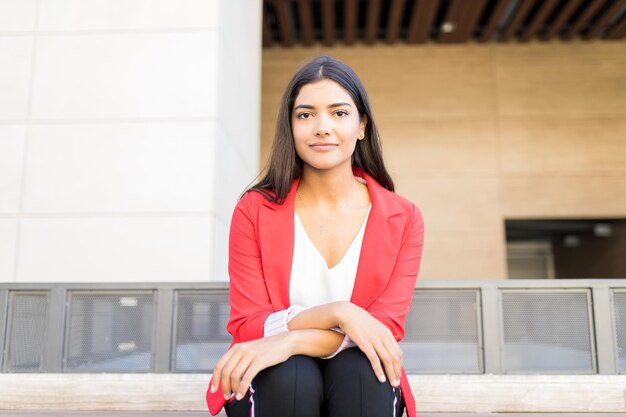 Jeune et professionnelle femme cadre portant une veste rouge alors qu'elle était assise à l'extérieur du lieu de travail