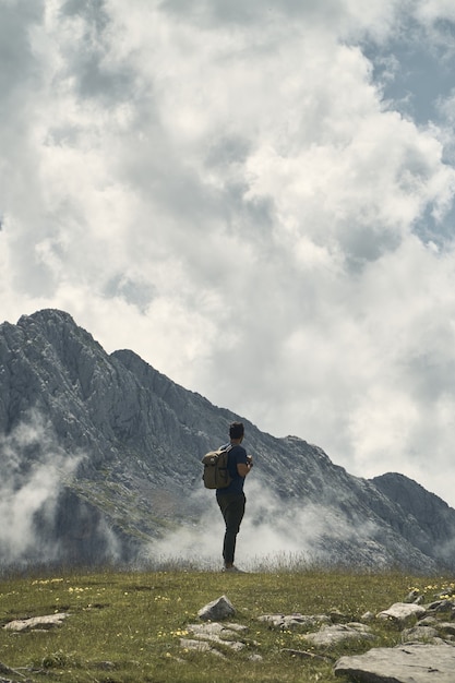 Jeune randonneur avec un sac à dos entouré de montagnes sous un ciel nuageux en Cantabrie, Espagne