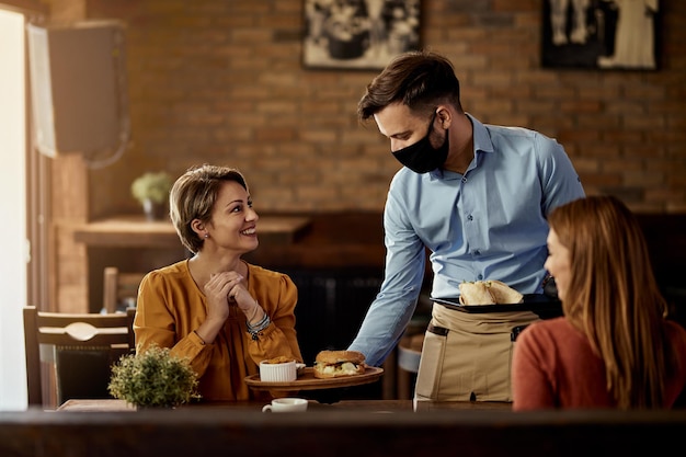 Jeune serveur portant un masque protecteur tout en servant de la nourriture à ses invités dans un restaurant