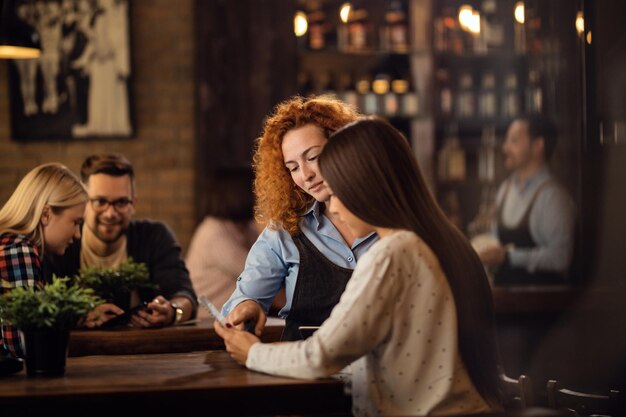 Jeune serveuse aidant une femme à choisir la commande à partir d'un menu dans un bar