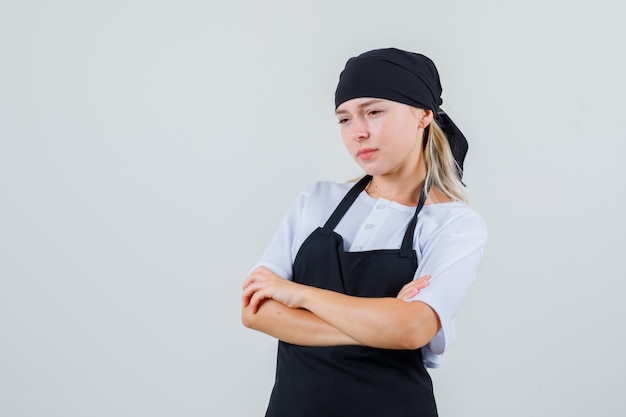 Jeune serveuse debout avec les bras croisés en uniforme et tablier et à la triste