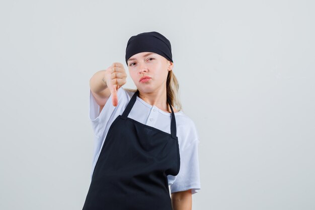 Jeune serveuse montrant le pouce vers le bas en vue de face uniforme et tablier.