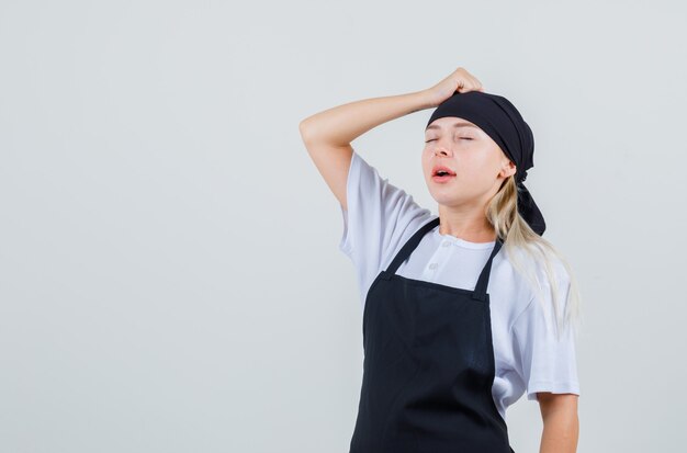 Jeune serveuse tenant le poing sur la tête en uniforme et tablier et à regret