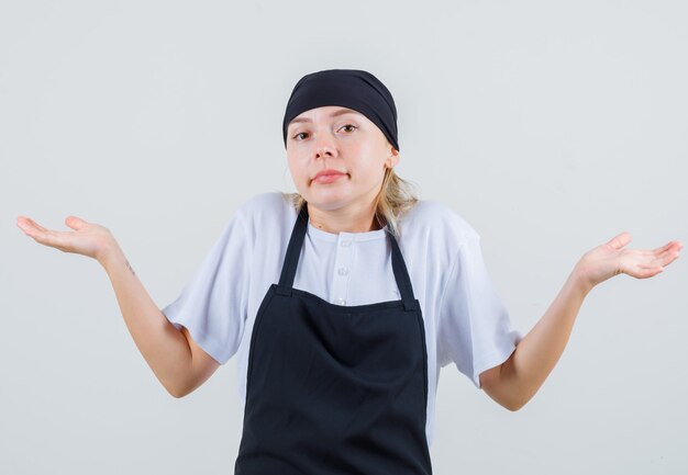 Jeune serveuse en uniforme et tablier montrant un geste impuissant et à la confusion