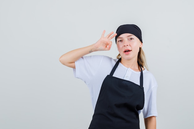 Jeune serveuse en uniforme et tablier montrant signe ok et à la satisfaction