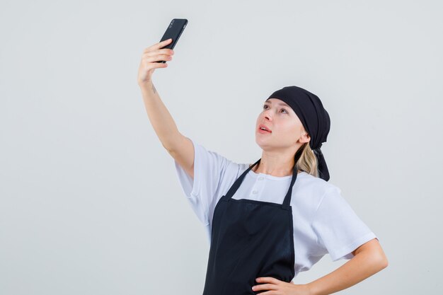 Jeune serveuse en uniforme et tablier prenant selfie sur téléphone mobile