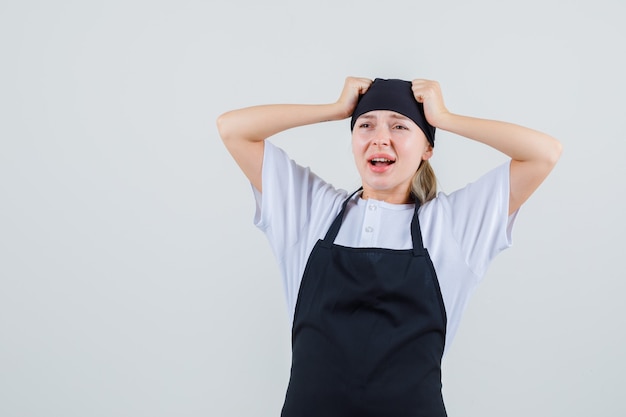 Jeune serveuse en uniforme et tablier tenant les poings sur la tête et à la triste