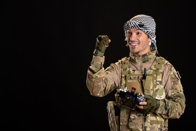 Jeune soldat en camouflage à l'aide de la télécommande sur mur noir