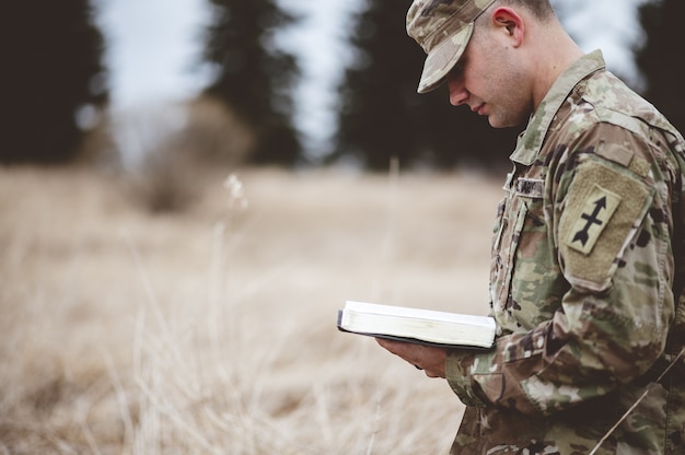 Photo gratuite jeune soldat lisant une bible dans un champ