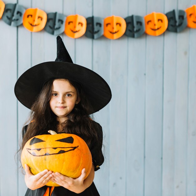 Jeune sorcière en costume tenant une grosse citrouille