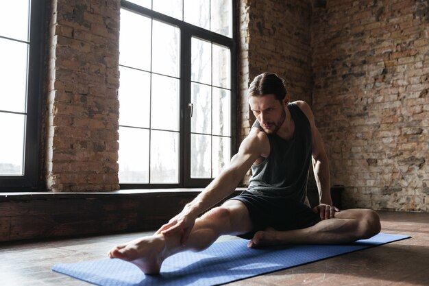 Jeune sportif concentré étirement des muscles sur le tapis de fitness