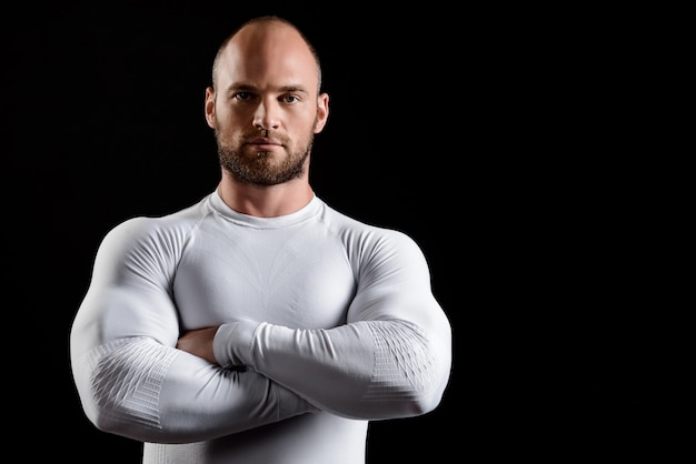 Jeune sportif puissant en vêtements blancs sur mur noir.