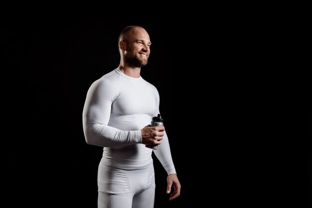 Jeune sportif puissant en vêtements blancs sur mur noir.