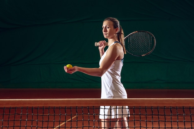 Jeune sportive professionnelle caucasienne jouant au tennis sur le mur du terrain de sport. Entraînement, pratique en mouvement, action. Puissance et énergie. Mouvement, publicité, sport, concept de mode de vie sain. Vue de face.