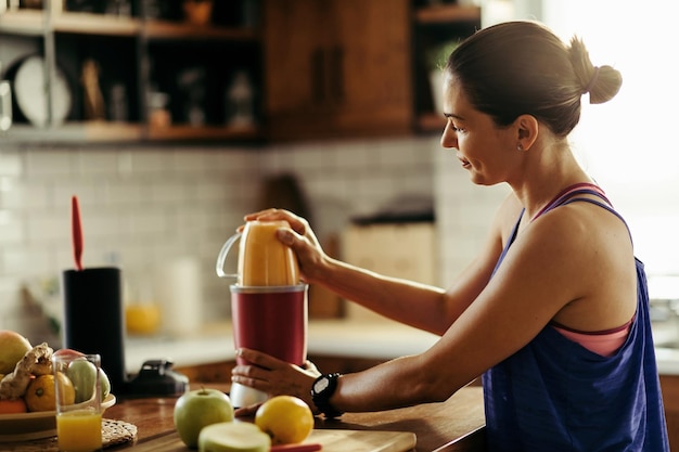 Jeune sportive utilisant un mixeur et préparant un smoothie aux fruits frais dans la cuisine