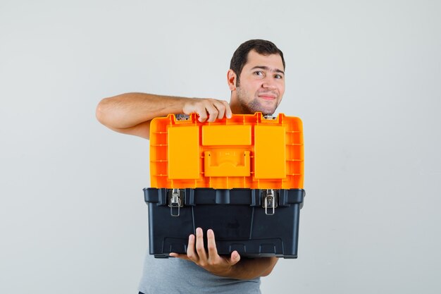 Jeune technicien en boîte à outils d'ouverture uniforme gris avec ses deux mains et l'air optimiste.