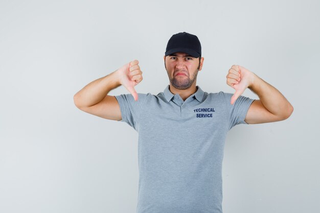 Jeune technicien montrant un double pouce vers le bas en uniforme et l'air déçu.