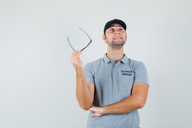 Jeune technicien tenant des lunettes en uniforme gris et à la réflexion.