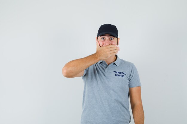 Jeune technicien tenant la main sur la bouche en uniforme gris et à la recherche d'excité.