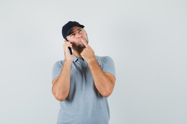 Jeune technicien en uniforme gris debout dans la pensée pose tout en parlant au téléphone et à la pensif.