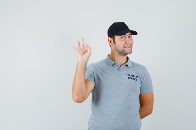 Jeune technicien en uniforme gris montrant un geste correct et l'air confiant.