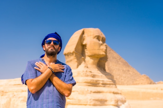 Un Jeune Touriste Près Du Grand Sphinx De Gizeh Vêtu De Bleu Et D'un Turban Bleu, D'où Les Miramides De Gizeh. Le Caire, Egypte | Photo Premium