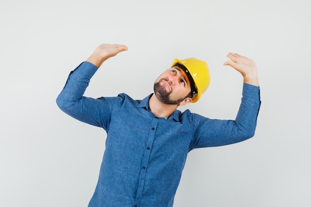 Jeune travailleur en chemise, casque levant les bras et inclinant la tête pour se défendre