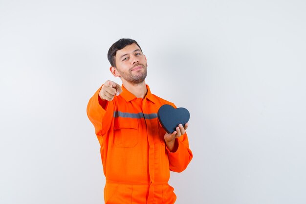 Jeune travailleur tenant la boîte présente, pointant vers l'avant en uniforme et l'air confiant.