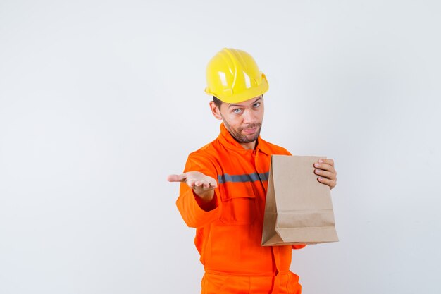 Jeune travailleur tenant un sac en papier, étirant la main en uniforme.