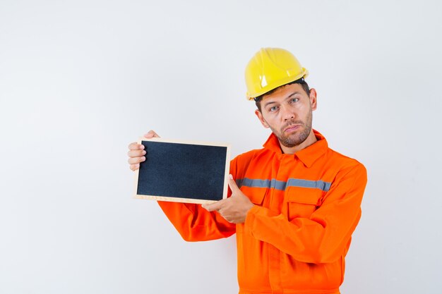 Jeune travailleur tenant tableau noir en uniforme, casque.