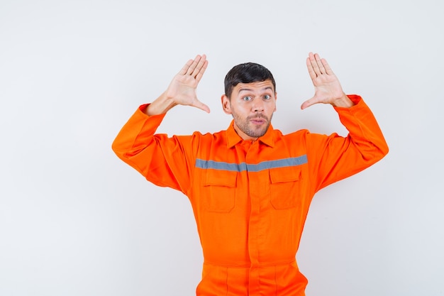 Jeune travailleur en uniforme levant les mains en geste de capitulation.