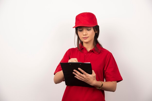 Jeune travailleur avec uniforme rouge et presse-papiers sur fond blanc.