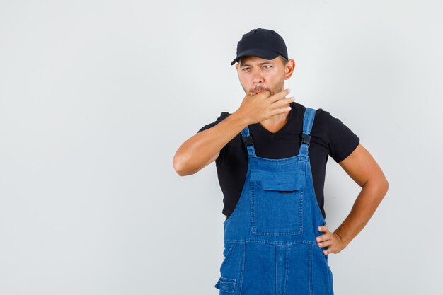 Jeune travailleur en uniforme sifflant avec la main sur la taille, vue de face.