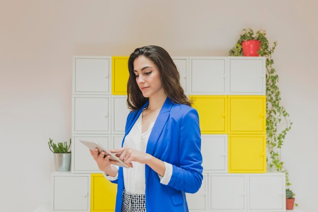 Jeune travailleur avec la veste bleue vérifiant sa tablette au bureau