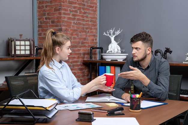 Jeune travailleuse et son collègue masculin assis à la table en train de réfléchir à une question importante au bureau