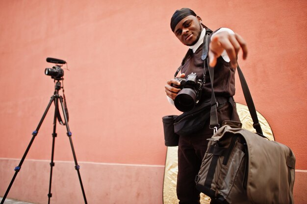 Jeune vidéaste afro-américain professionnel tenant une caméra professionnelle avec un équipement professionnel Caméraman afro portant du duraq noir faisant une vidéo