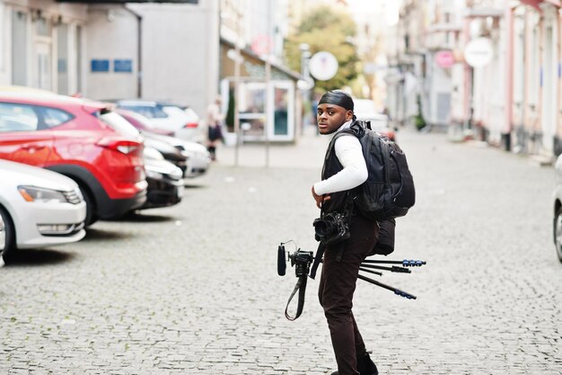 Jeune vidéaste afro-américain professionnel tenant une caméra professionnelle avec un équipement professionnel de trépied Caméraman afro portant du duraq noir faisant des vidéos