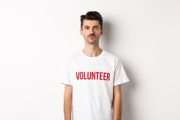 Jeune volontaire masculin sérieux en t-shirt blanc regardant la caméra, prêt à aider