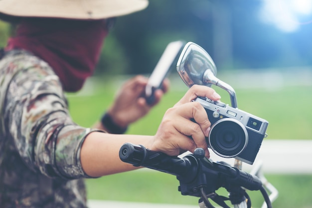 Jeune voyageur asiatique et photographe assis sur la moto de coureur de style classique tenant la caméra