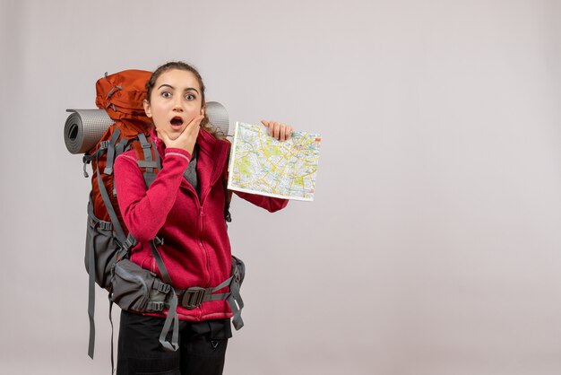 jeune voyageur perplexe avec un gros sac à dos tenant une carte sur fond gris