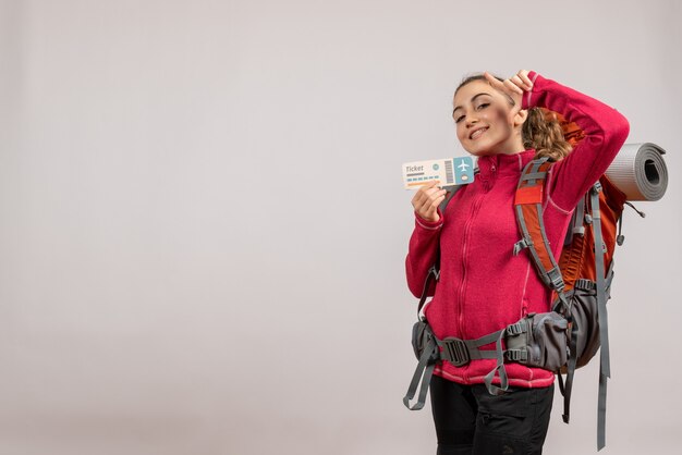 jeune voyageur souriant avec un gros sac à dos tenant un billet de voyage sur fond gris