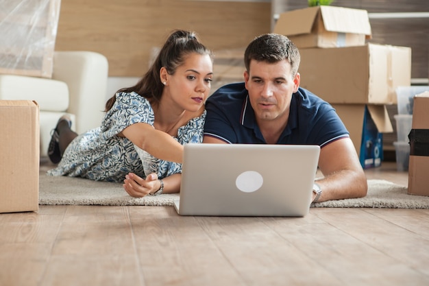 Jeunes adultes utilisant leur ordinateur portable dans le nouvel appartement pour de nouveaux meubles