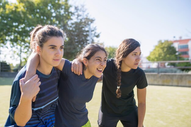 Jeunes amies sur le terrain de football. Des sportives dans différents uniformes regardent des compétitions, font des grimaces. Sport, loisirs, concept de mode de vie actif