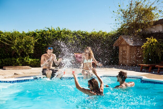 Jeunes amis gais souriant, riant, relaxant, nageant dans la piscine