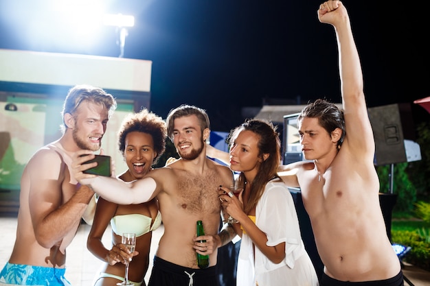 Jeunes amis gais souriant, se réjouissant, faisant selfie, se reposant à la fête