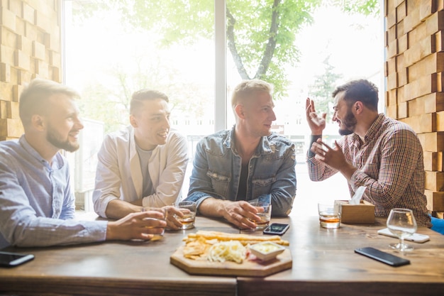 Photo gratuite jeunes amis masculins assis dans le restaurant en appréciant les boissons