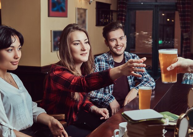 Jeunes amis multiraciaux au bar. barman donnant un verre de bière au client dans le pub.